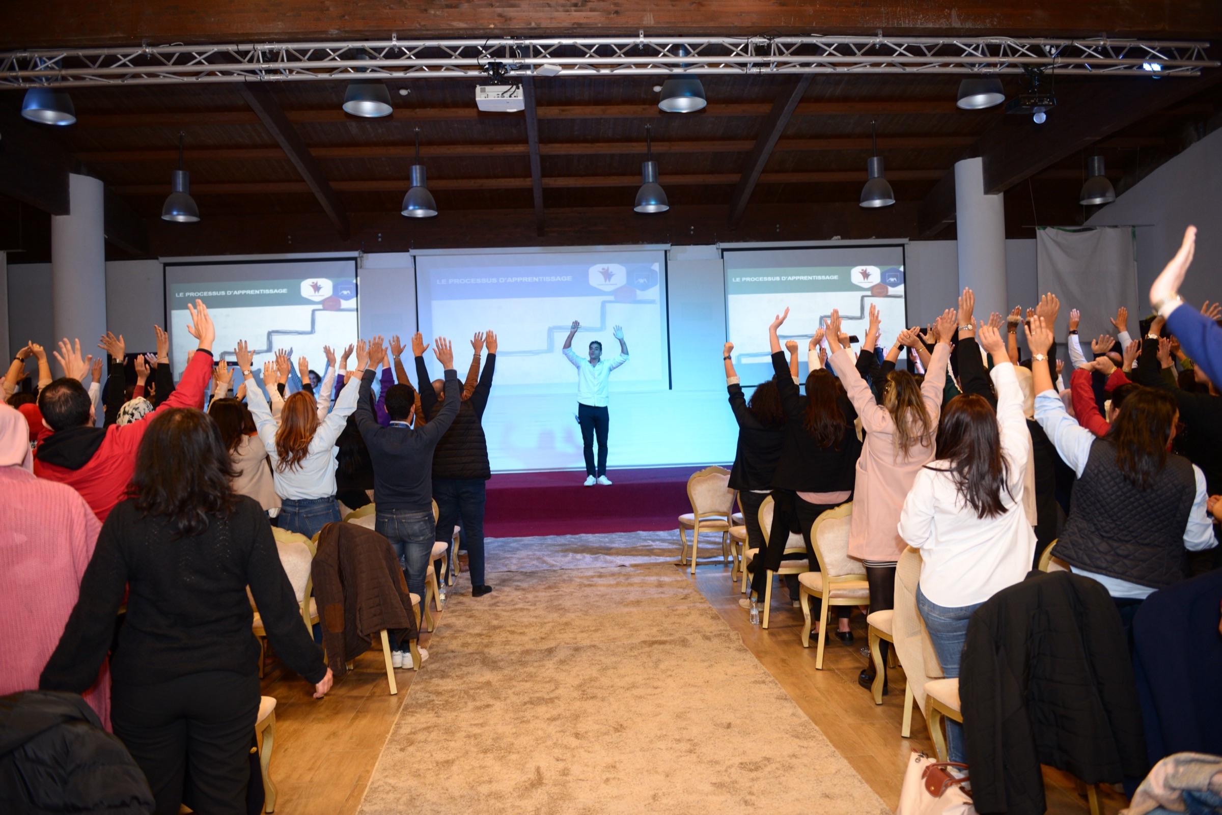 Participants debout, bras levés, lors d’une session Leadership Impact animée par Allal Bennani