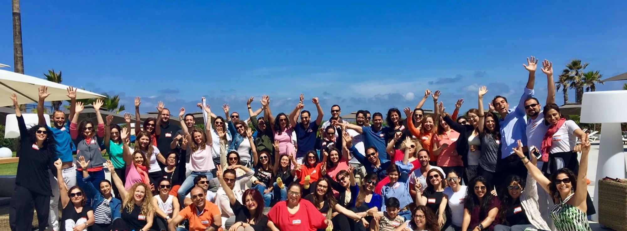 Grand groupe de participants souriants, bras levés, lors d’un séminaire Vieva en extérieur